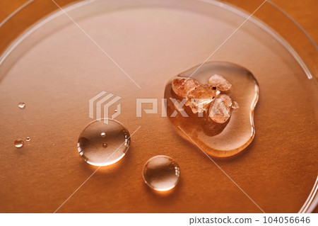 Three drops of liquid with pink salt on an orange background. 104056646