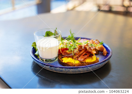 Very bright and healthy breakfast on a plate - bacon, egg, salad, tomato, cheese, a glass of yogurt. Very bright and healthy breakfast on a plate - bacon, egg, salad, tomato, cheese, a glass of yogurt. 104063224