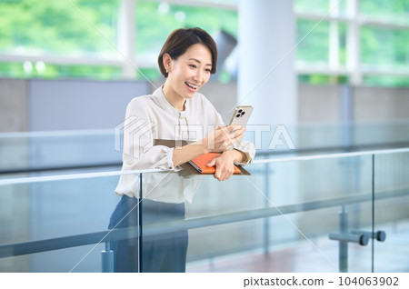 穿著商務休閒服的中層女商人在辦公室走廊裡看智能手機 104063902