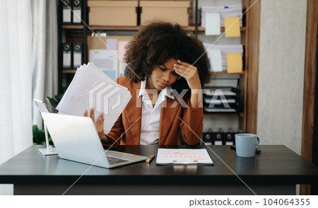 African business woman is stressed, bored, and overthinking from working on a tablet at the office. 104064355