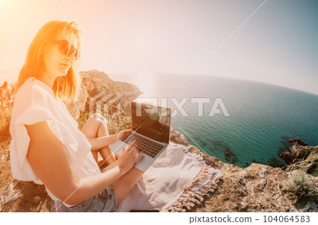 Woman sea laptop. Business woman working on laptop by sea at sunset. Close up on hands of pretty lady typing on computer outdoors summer day. Freelance, digital nomad, travel and holidays concept. 104064583