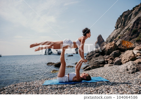 Woman sea yoga. Two Happy women meditating in yoga pose on the beach, ocean and rock mountains. Motivation and inspirational fit and exercising. Healthy lifestyle outdoors in nature, fitness concept. 104064586