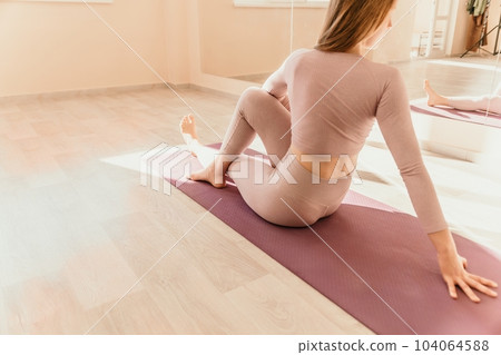 Young sporty woman, fitness instructor in pink sportswear doing stretching and pilates on yoga mat in the studio with mirror. Female fitness yoga routine concept. Healthy lifestyle and harmony. 104064588