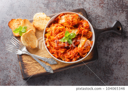 White fish stew with carrots and onions in spicy tomato sauce served with toast close-up on a wooden board. horizontal top view 104065346