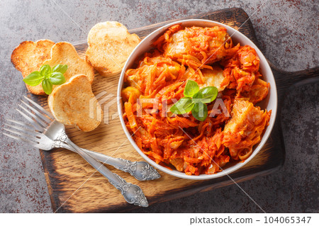 Homemade fish stew with vegetables in spicy tomato sauce served with toast close-up on a wooden board. horizontal top view 104065347