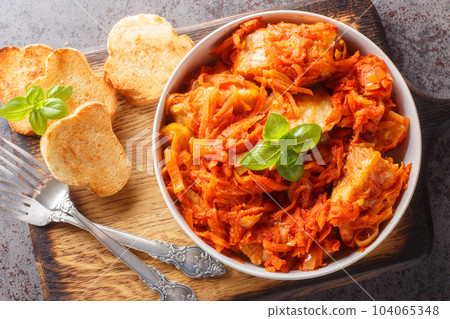 Delicious fish stew with vegetables in spicy tomato sauce served with toast close-up on a wooden board. horizontal top view Delicious fish stew with vegetables in spicy tomato sauce served with toast close-up on a wooden board. horizontal top view 104065348