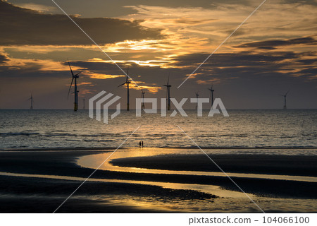 Fans of wind turbines spin over the sparkling sea. Dynamic clouds at sunset. Fans of wind turbines spin over the sparkling sea. Dynamic clouds at sunset. 104066100