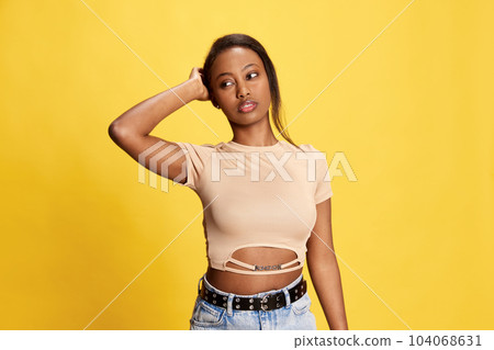 Portrait of young, beautiful african girl in casual clothes posing against yellow studio background Portrait of young, beautiful african girl in casual clothes posing against yellow studio background 104068631
