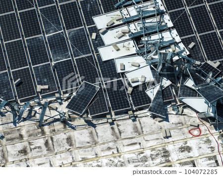 Broken down photovoltaic solar panels destroyed by hurricane Ian winds mounted on industrial building roof for producing green ecological electricity. Consequences of natural disaster 104072285