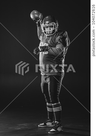 Portrait of a man in uniform for american football throws the ball on a black background. Monochrome.  104072616