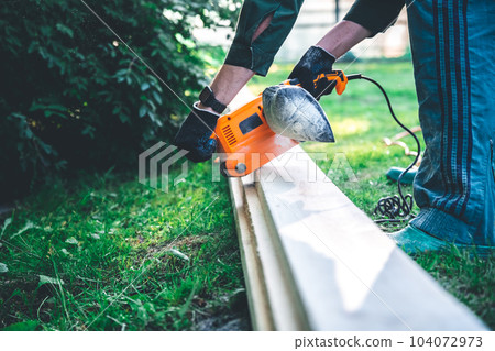 The man grinds the boards with a belt grinder, the electric tool for grinding and polishing the surface of the wooden board. The man grinds the boards with a belt grinder, the electric tool for grinding and polishing the surface of the wooden board. 104072973