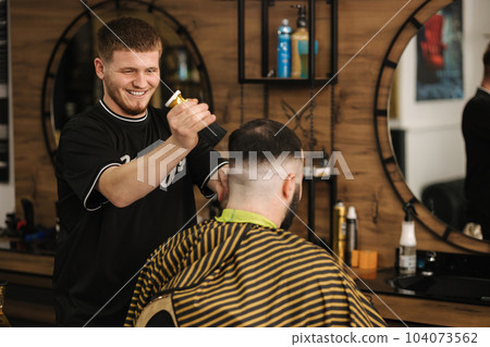 Confident bearded man visiting hairstylist in barber shop. Professional berber working Confident bearded man visiting hairstylist in barber shop. Professional berber working 104073562