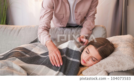 Home nap. Parent care. Unrecognizable woman covering plaid teenager girl sleeping on sofa weekend drowsing in light room interior. Home nap. Parent care. Unrecognizable woman covering plaid teenager girl sleeping on sofa weekend drowsing in light room interior. 104073583