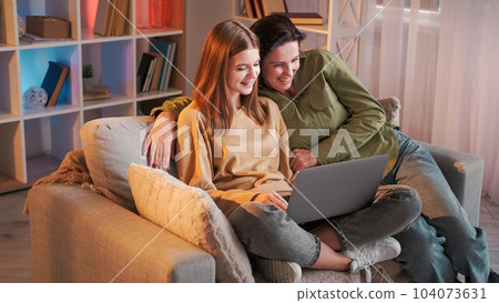 Sofa browsing. Family networking. Smiling woman teenage daughter watching movie online shopping surfing internet sitting sofa home interior. 104073631
