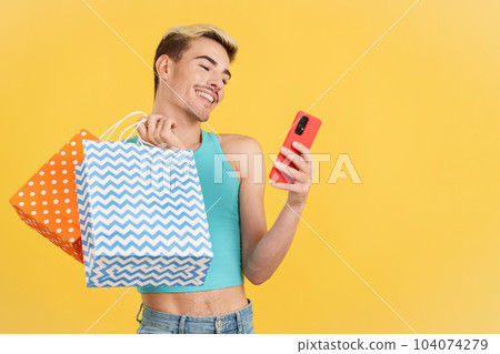Happy gay man using the mobile while holing shopping bags 104074279