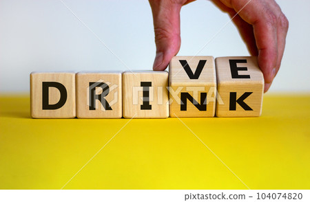 Drink or drive. Male hand flips a wooden cube and changes the inscription 'drink' to 'drive'. Beautiful yellow table, white background, copy space. Concept. 104074820