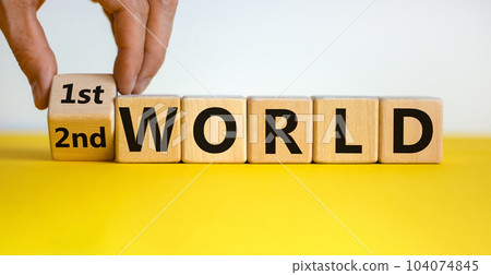 Male hand flips a wooden cube and changes the inscription '2nd world' to '1st world'. Beautiful yellow table, white background, copy space. Business concept. Male hand flips a wooden cube and changes the inscription '2nd world' to '1st world'. Beautiful yellow table, white background, copy space. Business concept. 104074845