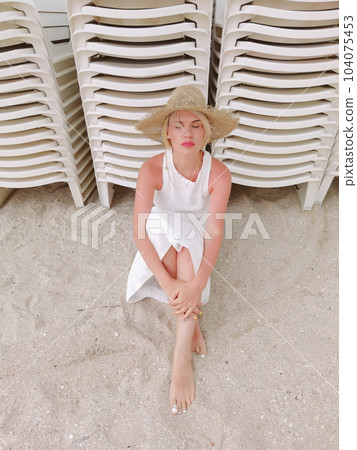 Portrait of fashion young woman wearing a straw hat. Sensual girl sitting on beach with copy space. Attractive girl looking at camera. Portrait of fashion young woman wearing a straw hat. Sensual girl sitting on beach with copy space. Attractive girl looking at camera. 104075453