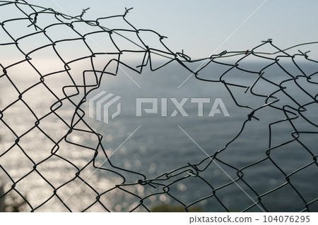 Hole in wired fence, made by tourista to see a sea view Hole in wired fence, made by tourista to see a sea view 104076295