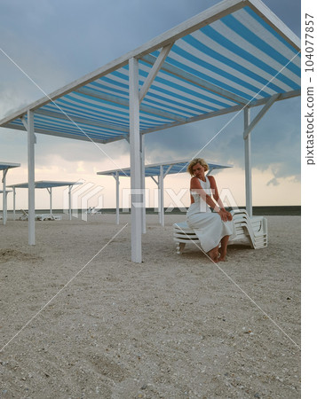 Portrait of blond young woman on empty beach wearing white dress and summer hat. Portrait of blond young woman on empty beach wearing white dress and summer hat. 104077857