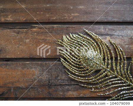 Golden peacock feather. Decorative gilded branch in the shape of a peacock's tail and eyelet. Wooden background. Festive decoration and beautiful carnival decor. Flat lay copy space. 104079099