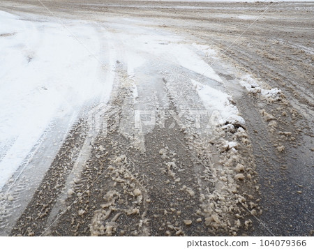 Roadside with a snowdrift. Difficult driving conditions. Wet slippery pavement with footprints. Dangerous ice. Muddy weather in winter. Car tire tracks. The work of municipal services for cleaning. 104079366