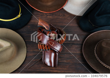 Gun with holster and gunbelt with old west hats on table. Top view. 104079576