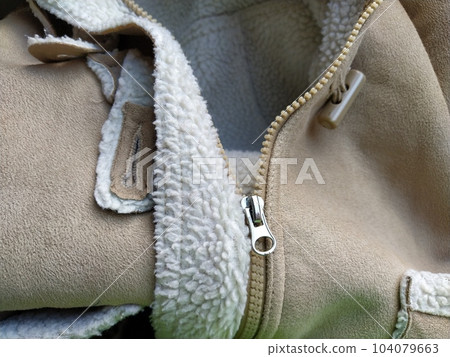 Suede outerwear. Overhead loops for buttons. Open zipper. Beige faux suede with sheepskin on the fold of a demi-season garment. seams in the material. Clothing industry and fashion Suede outerwear. Overhead loops for buttons. Open zipper. Beige faux suede with sheepskin on the fold of a demi-season garment. seams in the material. Clothing industry and fashion 104079663