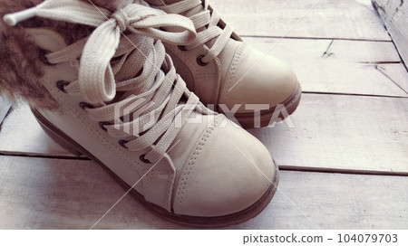 Beige children's boots with laces. Beautiful fashionable leather or suede shoes in a light shade on a wooden background. Exhibition of shoes. Shoes on display or shelf. Sale of shoes Beige children's boots with laces. Beautiful fashionable leather or suede shoes in a light shade on a wooden background. Exhibition of shoes. Shoes on display or shelf. Sale of shoes 104079703