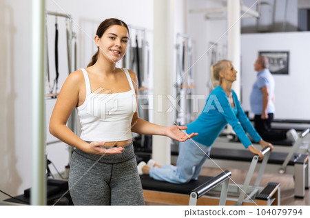 Portrait of young woman smiling at camera against group class in Pilates fitness studio 104079794