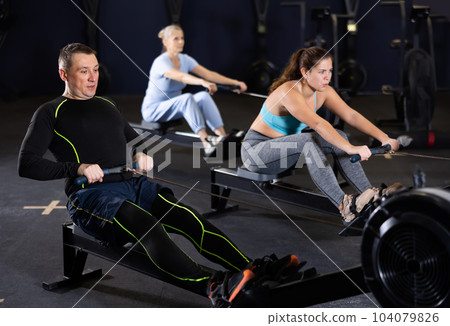 Athlete is engaged in the gym, man works on rowing simulator Athlete is engaged in the gym, man works on rowing simulator 104079826
