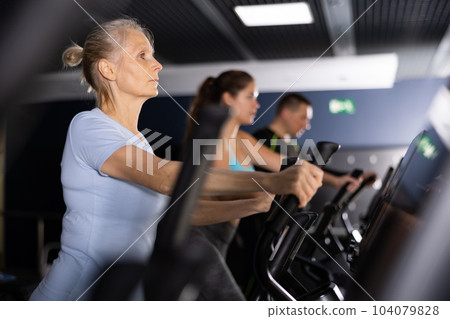Older sportswoman training at elliptical machine in gym Older sportswoman training at elliptical machine in gym 104079828