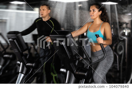 Athletic young woman exercising on an elliptical trainer in gym 104079840