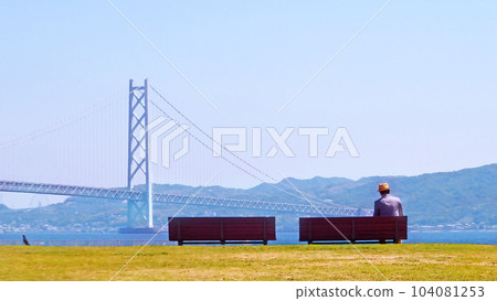 A gentleman reading a book on a bench Akashi Kaikyo Bridge background [horizontal composition] 104081253