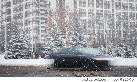 snowfall in the city, a car in blur on the road, snow-covered fir trees grow along the road snowfall in the city, a car in blur on the road, snow-covered fir trees grow along the road 104081549