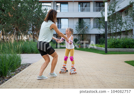 Mother helps daughter learn to roller skate.  104082757