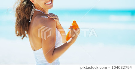 Smiling young woman on beach applying sun block creme 104082794
