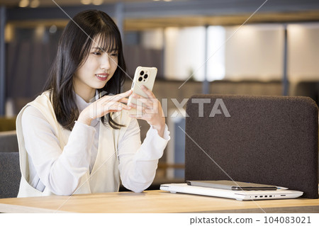 一位年輕女性在時尚的咖啡廳辦公室裡看著她的智能手機 104083021