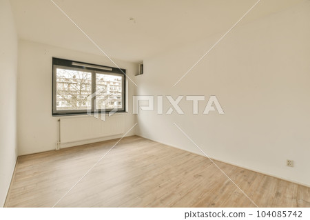 an empty room with wood floors and white walls, there is a large window in the wall to the right 104085742