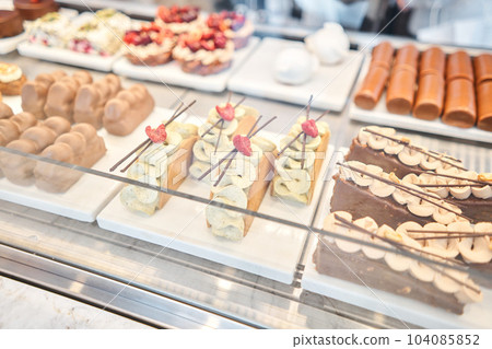 A variety of cakes covered with chocolate and decorated with pistachio mousse. A showcase in a pastry shop with delicious desserts with fresh berries and cream. Delicious pastries in the coffee shop. A variety of cakes covered with chocolate and decorated with pistachio mousse. A showcase in a pastry shop with delicious desserts with fresh berries and cream. Delicious pastries in the coffee shop. 104085852