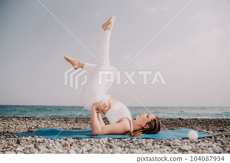 Woman sea yoga. Well looking middle aged woman with braids dreadlocks in white leggings and tops doing stretching pilates on yoga mat near sea. Female fitness yoga routine concept. Healthy lifestyle. 104087934