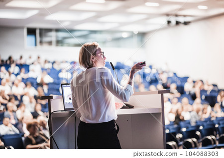 Female speaker giving a talk on corporate business conference. Unrecognizable people in audience at conference hall. Business and Entrepreneurship event 104088303