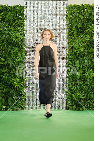 Middle aged woman in linen sundress walking on green carpet Middle aged woman in linen sundress walking on green carpet 104088327