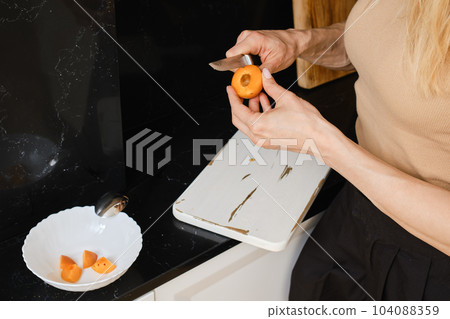 Closeup of woman cutting apricot into halves 104088359