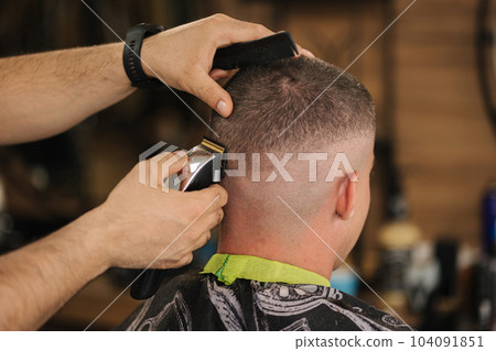 Back view of human hand hold trimmer and make hairstyle for man. Barbershop  104091851