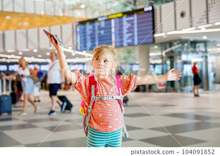 Little preschool girl at airport terminal. Happy child going on vacations by airplane. Smiling kid with passport and bag. 104091852