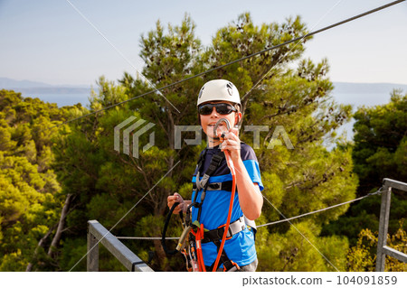 School boy preparing for zipline adventure. Happy active child put safety helmet on head. Summer fun with climbing in mountains. School boy preparing for zipline adventure. Happy active child put safety helmet on head. Summer fun with climbing in mountains. 104091859