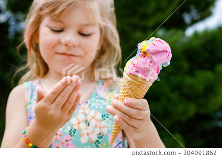 Happy preschool girl eating colorful ice cream in waffle cone on sunny summer day. Little toddler child eat icecream dessert. Sweet food on hot warm summertime days. Bright light, colorful ice-cream Happy preschool girl eating colorful ice cream in waffle cone on sunny summer day. Little toddler child eat icecream dessert. Sweet food on hot warm summertime days. Bright light, colorful ice-cream 104091862