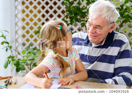 Happy positive cute little preschool girl and handsome senior grandfather painting with colorful pencils at home. Grandchild and man having fun together 104091926