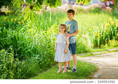 School kid boy and little sister, preschool girl playing together in park. Two happy children play and having fun sunny summer day. Siblings in love. Lovely sister and brother. 104091992